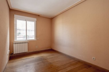 Boş oda kırmızımsı krem rengine boyanmış meşe ağacından zemin, alüminyum pencere ve radyatör.