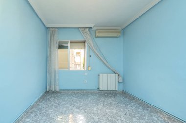 Boş daire, mavi boyanmış duvarlar, alüminyum radyatör, beyaz perdeler ve mermer görünümlü döşemeler.