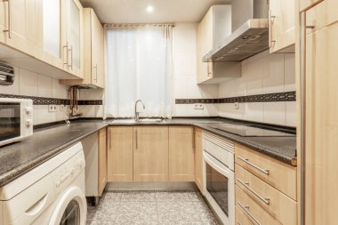 Square kitchen with light wood cabinets and black countertop with white appliances