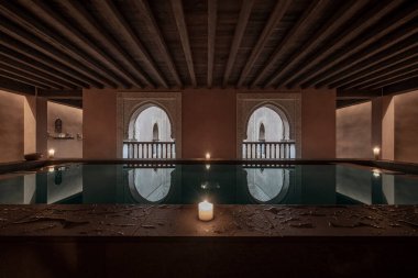 Symmetrical image of a pool of Arab baths with candles and balustrades with wood and numid arches