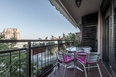 Terrace with awning and aluminum table and chairs overlooking a garden with trees
