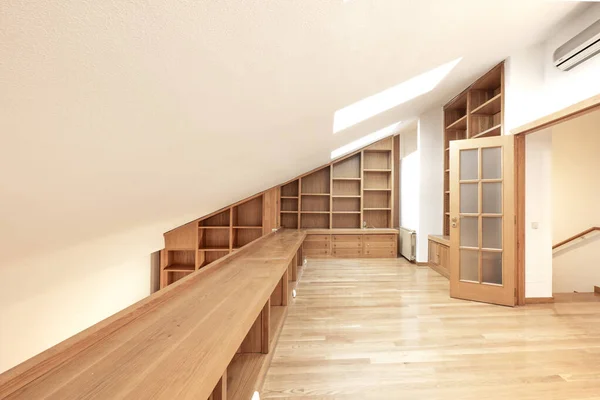 Room with sloping ceiling and oak wood bookcase with parquet floors