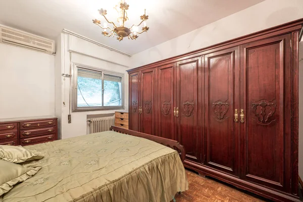 Bedroom in bedroom with vintage and kitsch furniture with a large mahogany wood multi-body wardrobe