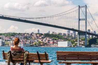 İstanbul Boğazı 'na bakan ahşap bir bankta dinlenen kızıl saçlı.