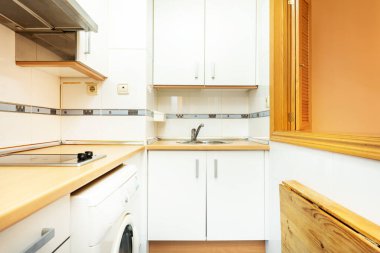 Hafif ahşap tezgahları ve beyaz dolapları olan küçük bir mutfak, Venedik tarzı ahşap pencere ve tezgah.