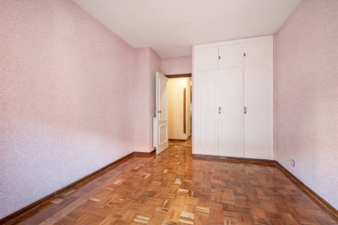 Pembe ve ahşap zemine boyanmış üç beyaz beden ve duvardan oluşan gömme dolabı olan bir oda.