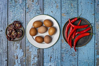 Çiğ yumurtalı tabaklar, mavi ahşap masada kırmızı biber.