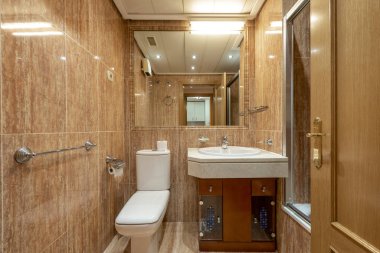 Meşe mobilyalı banyo, mermer tepeli beyaz porselen lavabo, duvara monte edilmiş ayna ve paslanmaz çelik şamdanlar.