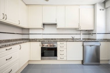Duvarları beyaz ahşap dolaplarla kaplı gri granit kaplamalı mutfak ve kenarları beyaz ve gri fayanslarla uyumlu.
