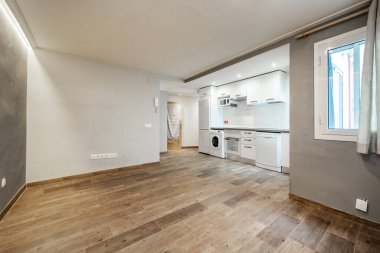 Kiralık bir stüdyonun bir tarafında beyaz dolaplar ve eşleşen aletler olan ahşap döşemeleri ve beyaz ve gri duvarları olan mutfak.