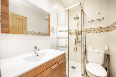 Geleneksel tuvalet ahşap mobilyalar, uzatılmış beyaz lavabo ve ekranlı kare duş kabini.