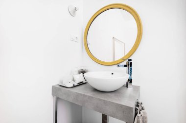 Çukur porselen lavabolu banyo ve dairesel altın çerçeveli ayna.