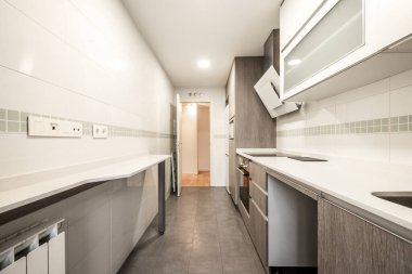 Modern ve uzun mutfak, gri ahşap mobilyalar, beyaz taş tezgah ve kenarlı fayanslar.