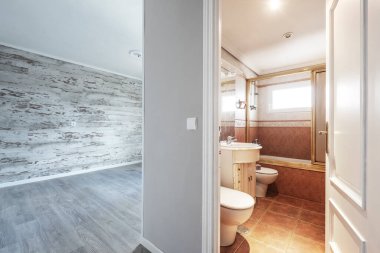 Kahverengi tonlarında duvar kağıdı olan boş bir oda ve beyaz duşlu ve tuvaletli takım elbiseli bir yıl.