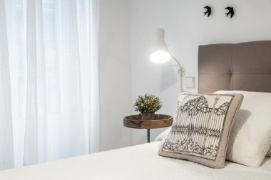 Yatak odası yatak başlığı, yastıklar, lamba ve beyaz perdenin yanındaki dekoratif parçalar.