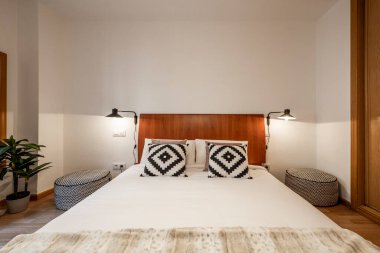 Büyük boy yatağın üzerinde ahşap bir yatak, bir tarafta tığ işi yastıklar ve Brezilya ahşap bir ekran var.