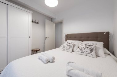 Klasik yatak odası beyaz ahşap sürgülü kapı dolabı döşeli yatak başlığı ve çiçek çizimli beyaz yastıklar.