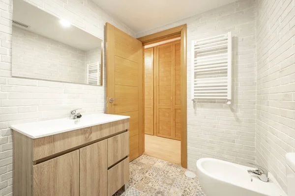 Exposed white brick bathroom with wood vanity, Venetian cabinet doors, cement tile flooring and white porcelain sink
