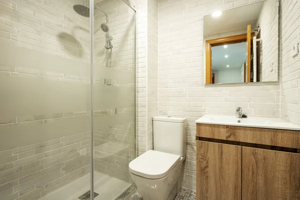 Bathroom with exposed white brick walls with wooden vanity, shower with glass partitions, hydraulic tile floors and white porcelain sink