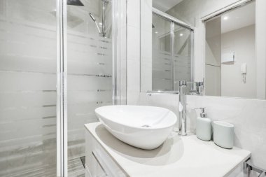 Kabuk şeklinde beyaz porselen lavabo. Duş var, duvara monte edilmiş ayna var.