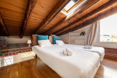 Tavan arasında, parke döşemeleri, ahşap kirişleri ve solaryum terasına erişimi olan eğimli tavanlı bir oda.