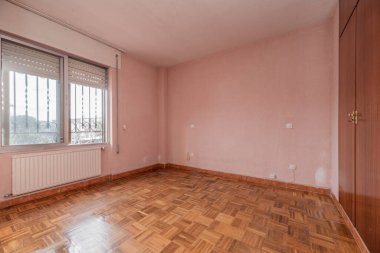 Boş yatak odası pembe boyalı duvarlar, ızgaralı alüminyum pencere ve ahşap kapılı gardırop.