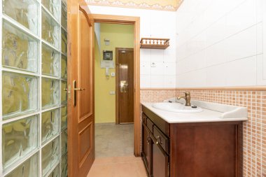 Koyu ahşap mobilyalı güzel bir banyo, beyaz mermer kapaklı, şeffaf cam asfalt duvarlı ve kahverengi fayanslı.