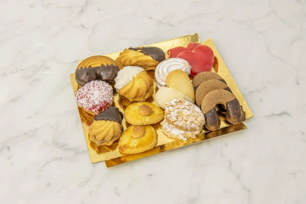 The assorted homemade butter cookies or the tea cookies are delicious since the butter and the touch of vanilla give them a tremendous flavor, these are on a golden tray and white marble table