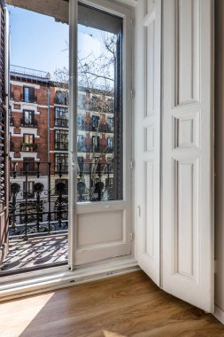 Sokağa bakan eski bir binanın balkonunda beyaz boyalı ahşap pencereler ve panjurlar var.