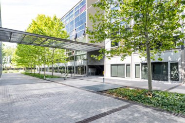 Önü cam yüzeyi ve iç geçidi ağaçlı bir bahçesi olan bir konut binasının ön cephesi.