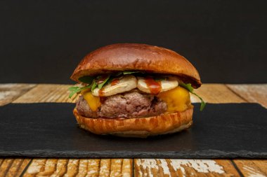 Siyah bir tabakta roka, mantar, barbekü sosu ve çedar peyniri ve boyanmamış ahşap masa.