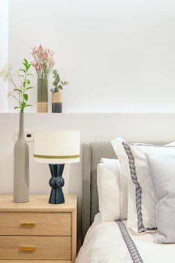 Döşeme döşenmiş yatak başlığı, alçıdan yapılma, çiçek vazoları, mavi lambalı hafif ahşap komodinlerle döşenmiş ve bir sürü yastıkla birlikte.