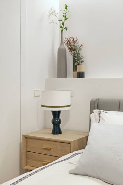 Döşeme döşenmiş yatak odası başlığı, alçı tahta inşaatına eklenmiş vazolar ve mavi lambalı hafif ahşap komodiniyle.