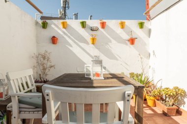 Endülüs tarzı renkli tencereleri olan beyaz bir teras duvarı, güneşli bir günde yerde daha fazla tencere ve sandalyeli ahşap bir masa.