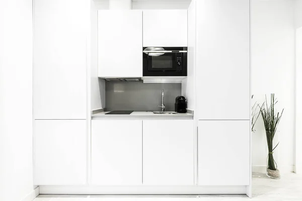 コーヒーマシンの横に黒い電子レンジ セラミックハブとシンク付きの白い家具キッチン — ストック写真
