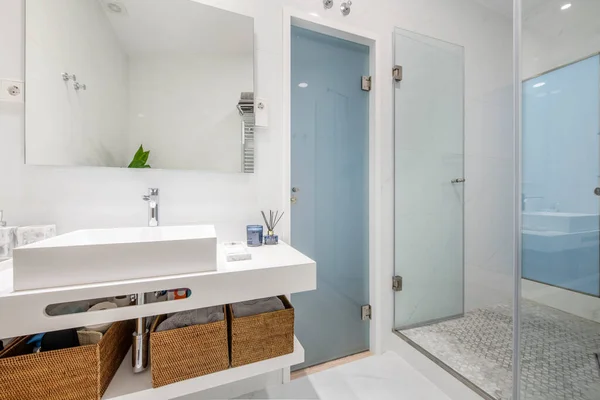 bathroom with white porcelain fixtures white tiled walls and marble floors and stainless steel heated towel rail and shower stall with glass partition