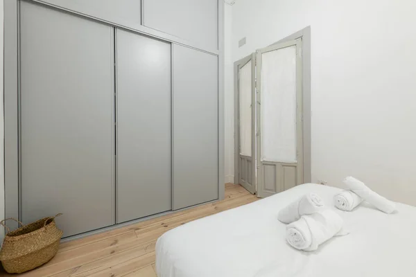 有白色被褥的卧室 床上铺有卷曲的毛巾 灰色滑动门柜和带有松木地板的木门 — 图库照片