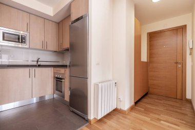 Ahşap renkli dolaplarla donatılmış açık mutfak, gri taş tezgah ve meşe parke döşemeli bir stüdyo dairesindeki paslanmaz çelik aletler.