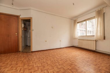 Sintasol benzeri ahşap zeminli boş oda, parmaklıklı alüminyum pencere ve beyaz perdeler ve beyaz alüminyum kalorifer ve alçı pervazlı tavan.