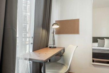 Beyaz sandalyeli çalışma masaları, siyah lamba ve yatak odasındaki duvarda bir ayna.