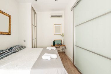 Dolabında cam kapılar, mavi yastıklar, altın çerçeveli ayna ve klima olan bir oda.