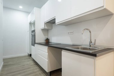 Siyah tezgahlı yeni takılmış mutfak, gri ahşap zemin, paslanmaz çelik lavabo, uygun musluk ve konveksiyon fırını.