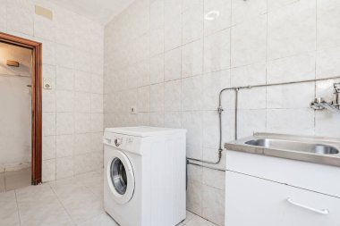 Çamaşır makinesi, paslanmaz çelik lavabo, taş kaplama döşemeler ve uyumlu duvarlarla dolu bir oda.