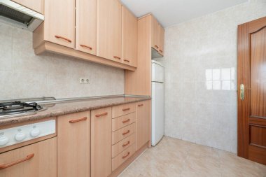 Ahşap mobilyalı mutfak ve uygun çekmeceler pembe granit tezgahlı beyaz buzdolabı hafif fayanslı ve krem taş kaplamalı döşemeli ahşap kapılı