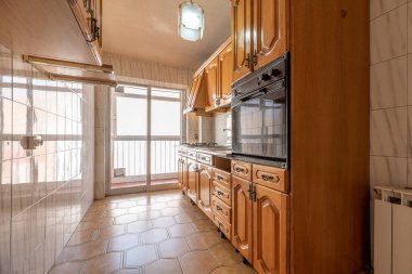 Sütunlarında gri kapılar olan ahşap mobilyaları ve parlak siyah tezgahı olan mutfak.,