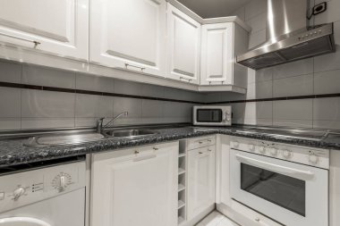 Mutfağın köşesinde beyaz mobilyalar, taklit mermer tezgah kuvars ve uyumlu aletler var.