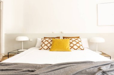 Kral yatak başlıklı yatak odası, yastıklı yan masalar, çift beyaz lambalar ve uyumlu yan masalar.