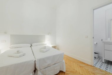 Çift kişilik yataklı yatak odası, beyaz çarşaflar, yataklarda banyo havluları ve beyaz komodinli yatak odası.