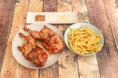 Kızarmış tavuk, patates kızartması ve ahşap masada sosla ikiye bölünmüş.