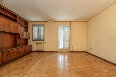 Ahşap duvar rafı odası, alüminyum pencere ve kalorifer ızgarası, krem renkli boyalı duvarlar ve tavanda alçı pervazla kaplı terasın çıkış kapıları.